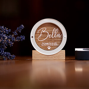 Round white and oak dog fur display keepsake named Bella on a polished wooden table with lavender on a dark background.